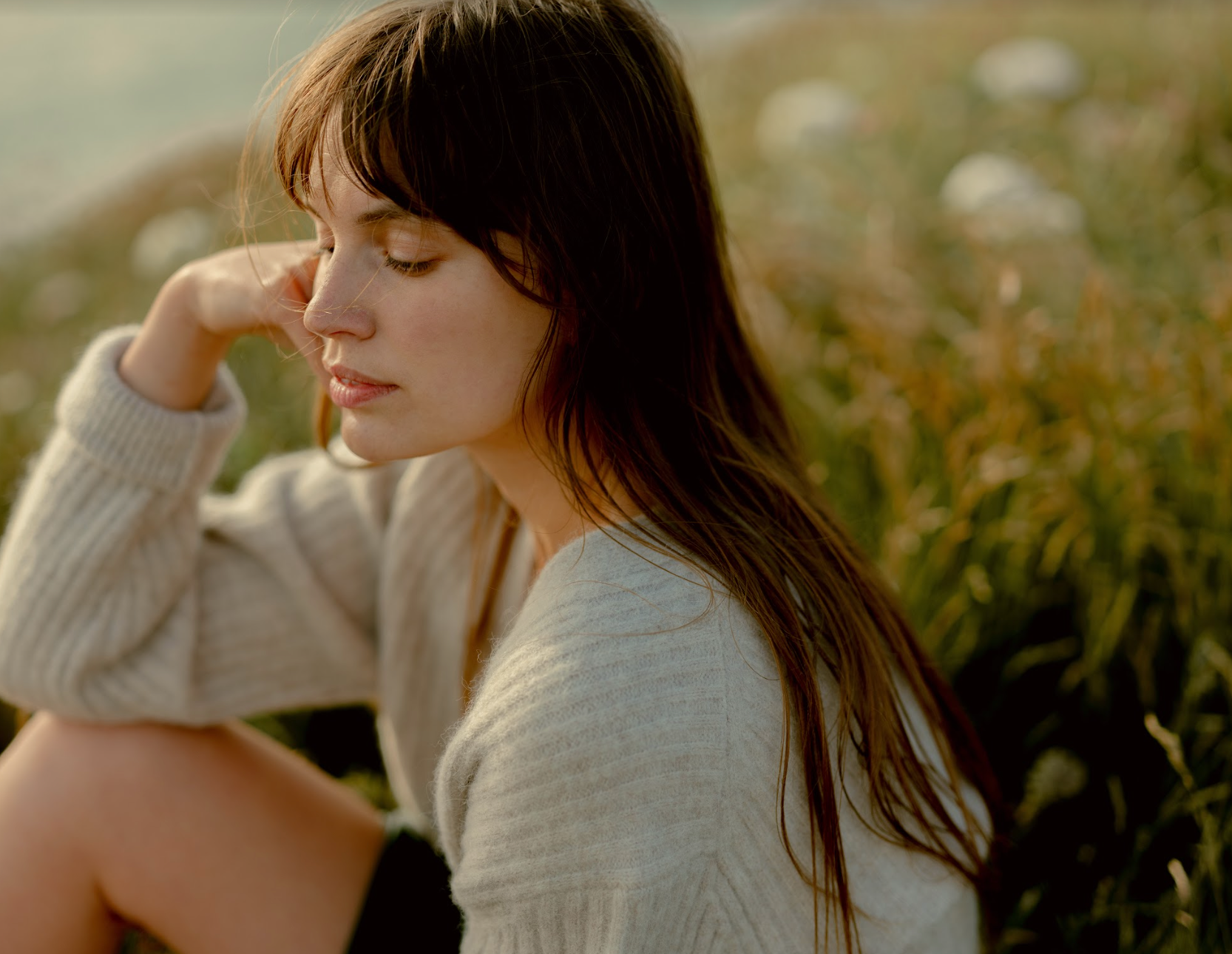 Woman sitting amongst grass with her eyes closed