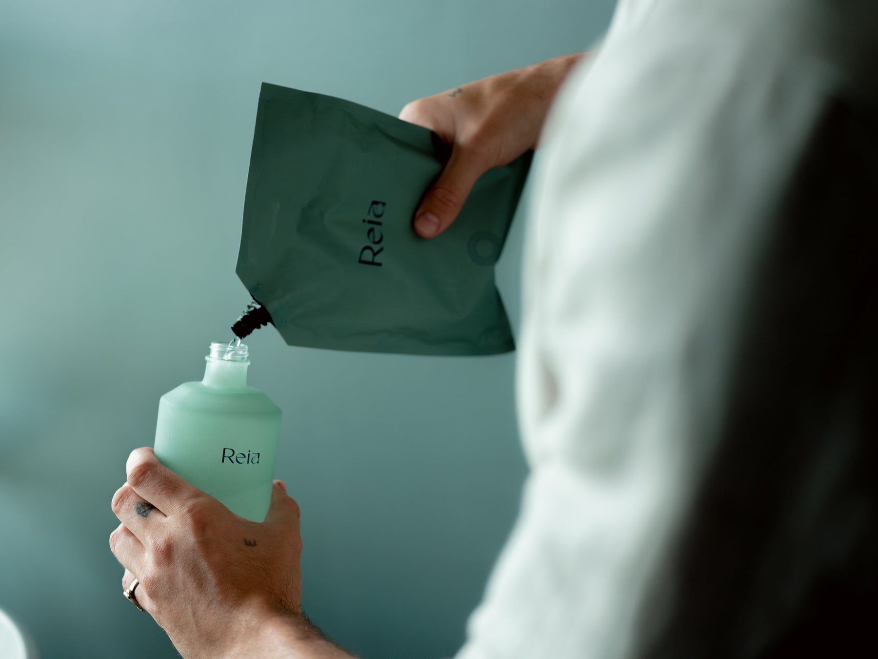 Man pouring a refill pouch into a Reia bottle